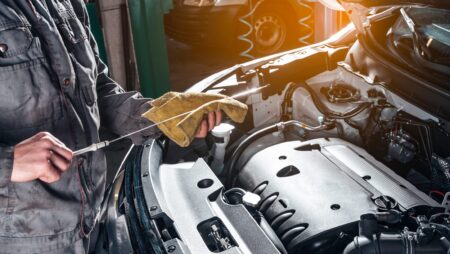 Auto shop worker under car hood checking oil