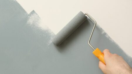 Gray paint being applied to white wall with roller brush