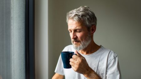 Mature man drinking coffee by window at home