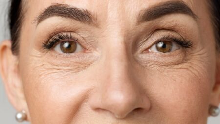 Closeup portrait of middle aged woman face with brown eyes over grey background. Model looking at camera.