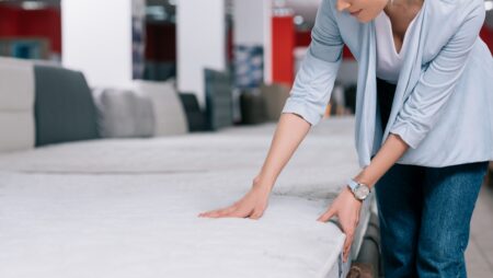 partial view of woman touching orthopedic mattress in furniture shop