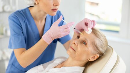 Cosmetologist making injections to forehead of elderly female patient