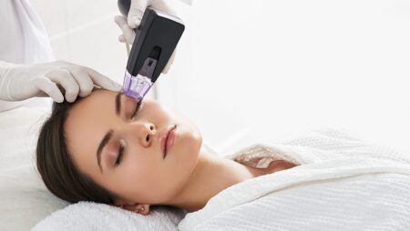 Brown haired woman receiving radiofrequency lifting procedure around eyes for her face skin rejuvenation at aesthetic cosmetology center