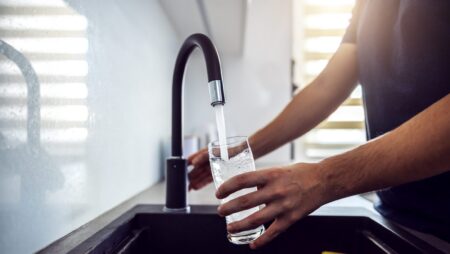 Close up of young man pouring fresh water from kitchen sink. Home interior.
