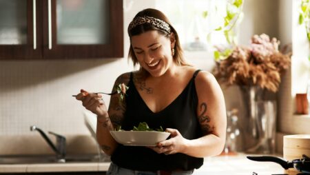 Woman, diet and person eating salad in her home kitchen and is happy for a meal with nutrition or healthy lunch. Smile, food and young female vegan in her apartment or house and eat vegetables