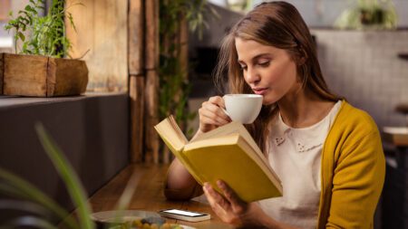 Woman reading book while drinking coffee