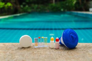 Pool maintenance tools lined on pool edge with chlorine tablet, water test kit, reagent bottles and floating dispenser