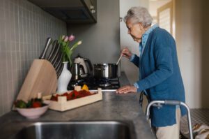 CarePlus Home Health Happy senior woman cooking in the kitchen. Gradmother making jam from fresh strawberries.
