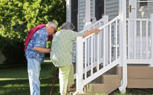 CarePlus Home Health Elderly senior couple arriving home. He is helping her climb slowly up their back porch steps.